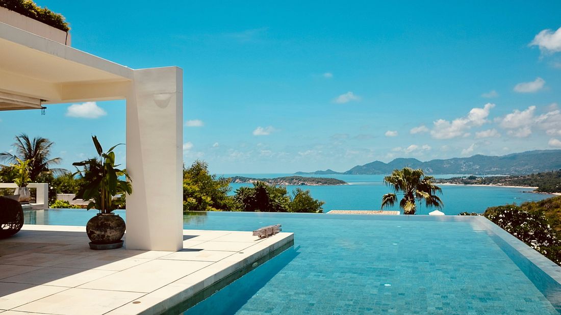 Infinity pool deck overlooking a bay, lined with palm trees